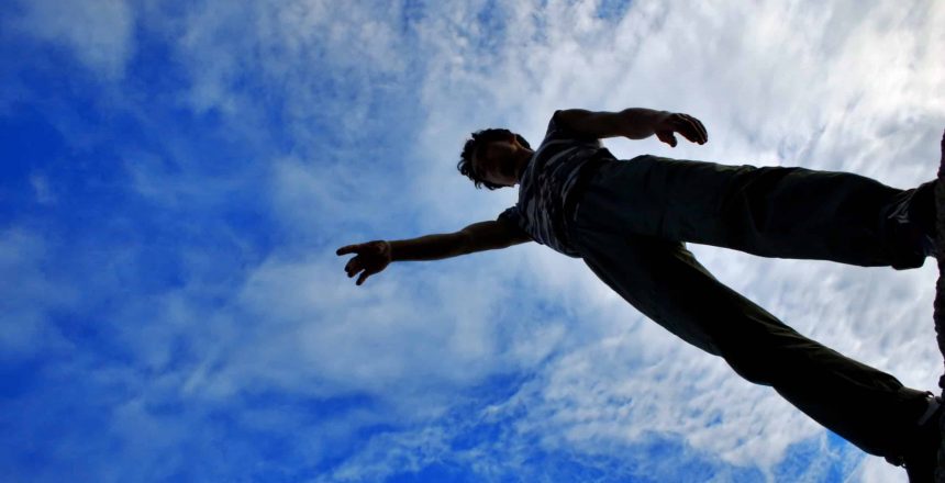 The young man is standing on a blue sky background pointing his hand ahead